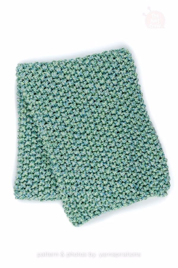 A folded knitted blanket with a bumpy texture, made of light mint green yarn speckled with bits of blue and dark green, resting on a plain white background, featured in a knitting roundup from https://www.theknitcrew.com/.