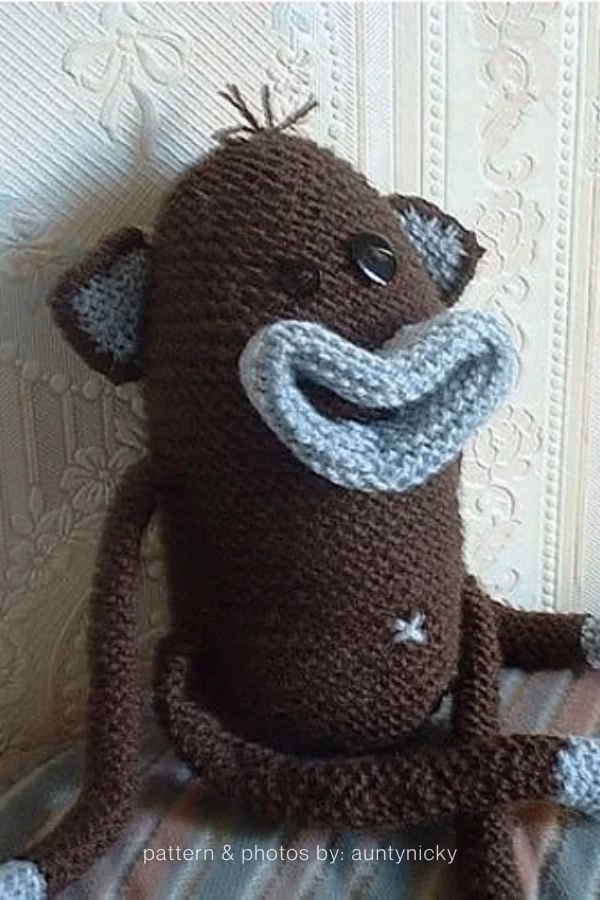 A handmade, dark brown knitted monkey plush with big button eyes and a wide, light blue knitted smile. Curated by Ariana of TheKnitCrew.