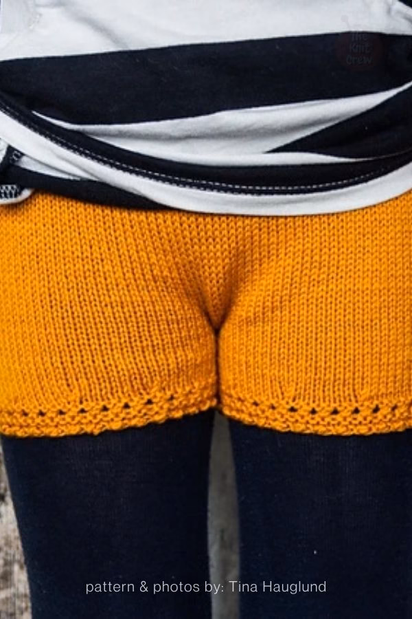 A close-up view of vibrant mustard-yellow knitted adult shorts featuring a delicate eyelet lace pattern along the bottom edges. Curated by Ariana of TheKnitCrew.
