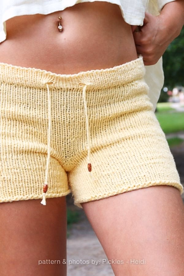 A close-up view of light yellow knitted adult shorts featuring a drawstring waist with small wooden beads. Curated by Ariana of TheKnitCrew.