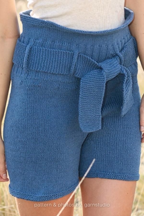 A close-up view of high-waisted blue knitted adult shorts with a thick, matching tied belt at the waist. Curated by Ariana of TheKnitCrew.
