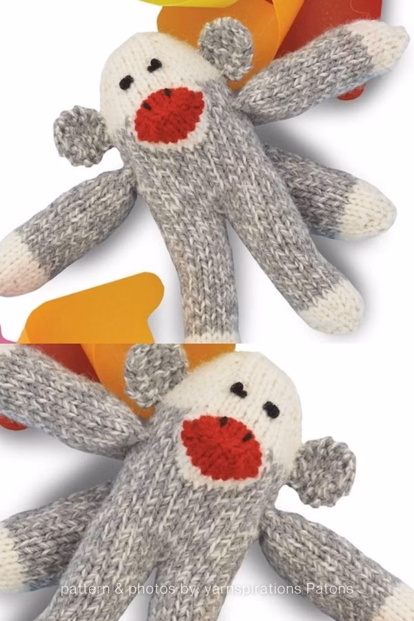 A close-up view of a classic grey heather knitted sock monkey plush with white paws, a cream head, and a vibrant red mouth. Curated by Ariana of TheKnitCrew.