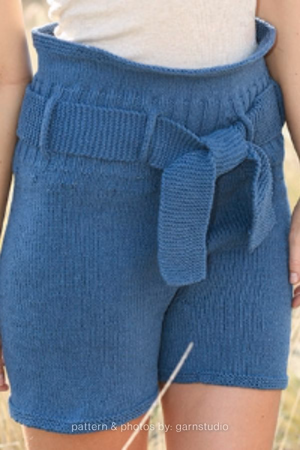 A close-up view of high-waisted blue knitted adult shorts with a thick, matching tied belt at the waist. Curated by Ariana of TheKnitCrew.