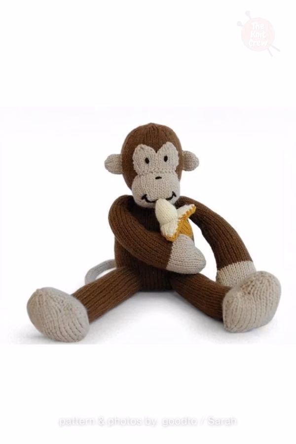 A solid brown knitted monkey plush sitting down while holding and eating a small yellow and white knitted banana. Curated by Ariana of TheKnitCrew.